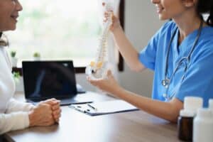 Female doctor discussing cervical fusion surgery with an elderly patient experiencing herniated disc deterioration from prolonged work hours.