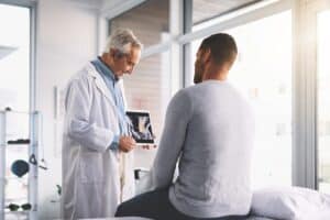 Doctor reviewing a spinal X-ray with a patient on a tablet, discussing posterior lumbar fusion surgery for spine stabilization and pain relief.