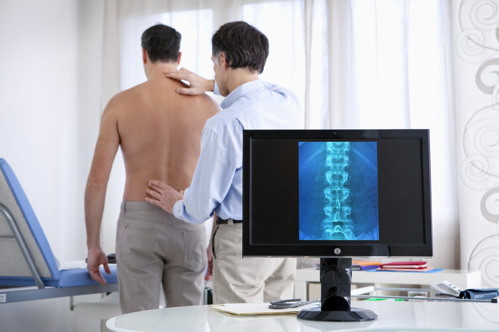 Male patient in consultation with an orthopedic doctor reviewing an X-ray for lumbar fusion surgery, focusing on spine care, back pain treatment, and potential rheumatology involvement for joint and musculoskeletal conditions.