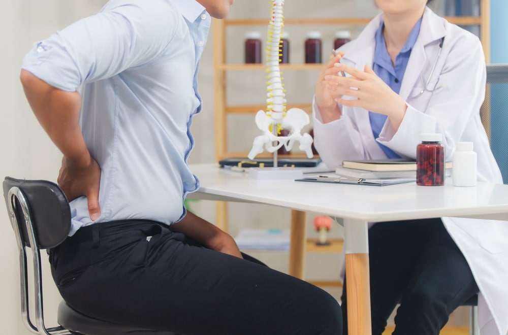 Orthopedic doctor explaining posterior lumbar fusion using a spinal model, highlighting treatment for spinal disorders, chronic back pain, and lumbar conditions in a spine care or chiropractic setting.