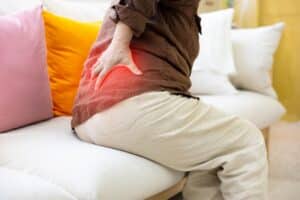 An elderly woman expresses visible discomfort while holding her lower back, indicating pain associated with a herniated disc