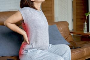 Woman experiencing sciatica pain, holding her lower back as discomfort radiates to the buttock, highlighting issues from bad posture and nerve irritation.