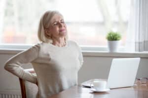 Woman sitting at desk holding her lower back in pain from herniated disc.