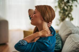 Woman holding her neck and shoulder while experiencing cervical pain.